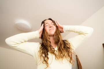 Fototapeta premium Young woman with dizziness holding hands on her head standing in living room at home, tired female with closed eyes with strong headache, vertigo, low blood pressure, vestibular, brain pain, low-angle