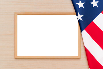Empty frame with white sheet and copy space on a light wooden table next to an American flag for patriotic holidays and congratulations on the American Independence Day.