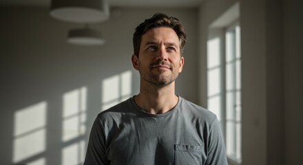 Young man gazing thoughtfully in a sunlit room with shadows and minimal decor