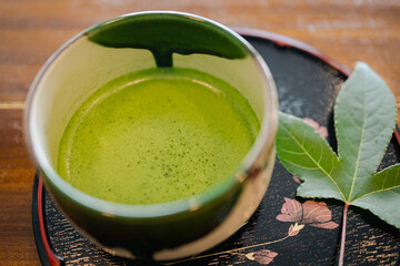 Green tea cup tea leaf wooden table black tray floral design hot beverage frothy tea traditional drink healthy drink natural ingredient ceramic cup close up fresh leaf herbal tea Asian culture tea