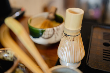 Traditional bamboo tea whisk with ceramic bowl and wooden table, used for preparing matcha tea in...