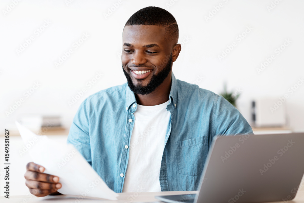 Poster millennial black freelancer man working with papers at desk in home office. smiling african american