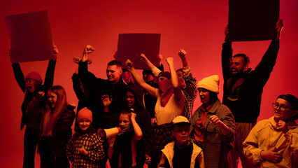 A diverse group of people holds protest signs with raised fists under red lighting. Concept of...