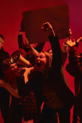 Protesters use a megaphone to shout slogans against a vivid red backdrop, symbolizing struggle and...