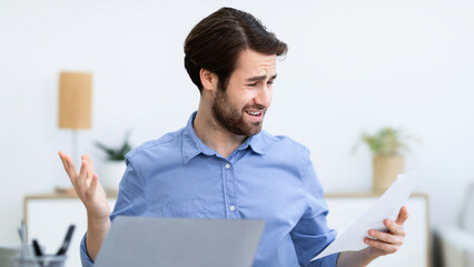 Displeased Businessman Looking At Smartphone Reading Negative Message Sitting At Laptop In Modern...