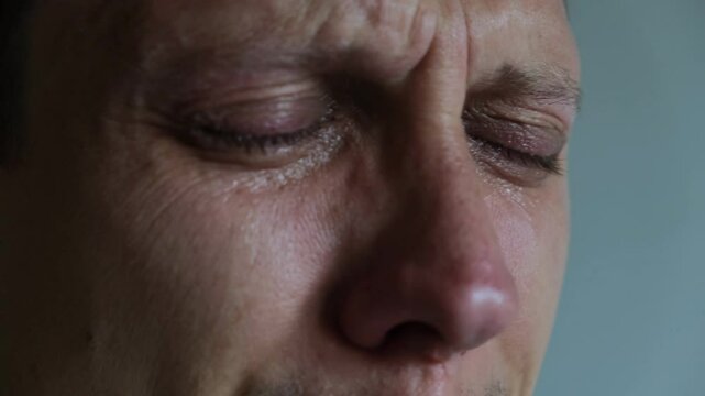 Young man talking and crying with eyes closed. Emotional close-up. Sadness, pain, inner struggle on neutral background