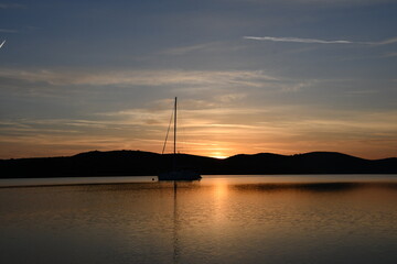 Serene Sunset Over Calm Waters with Sailing Boat in the Background