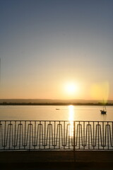 Serene Sunset over Tranquil Waters with a Silhouette of a Boat and decorative railing