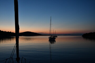Serene Sunset Over Calm Waters with Sailboats Silhouetted Against the Horizon