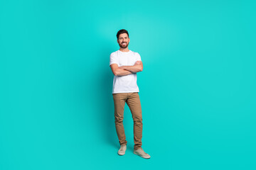 Confident young man standing with arms crossed against a vibrant turquoise background in stylish...