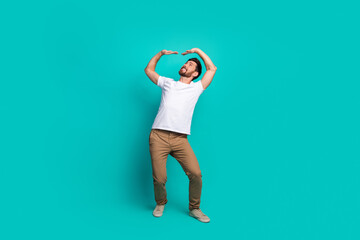 Cheerful young man posing stylishly in casual outfit on a teal background, expressing joy and...
