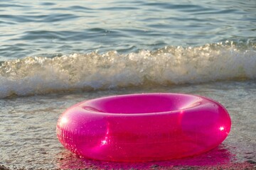 Pink plastic swim ring floating by the blue sea summer background
