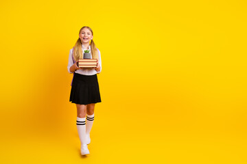 Fototapeta na wymiar Cheerful schoolgirl standing against yellow background holding books and a small plant, representing education, joy, and learning