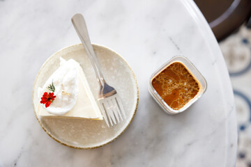 Cup of milk dirty coffee with a piece of coconut cake on white marble table by the window.