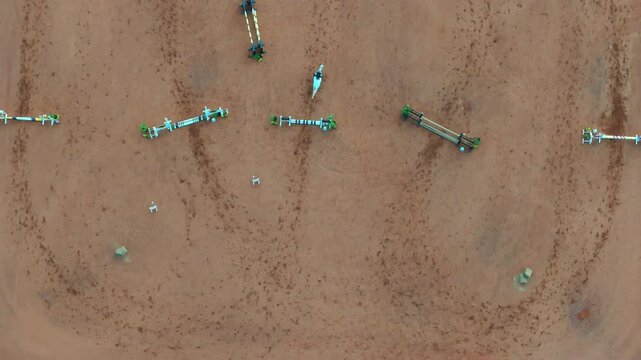Overhead drone view of a reddish equestrian training arena showing horse track marks and jumping fences arranged in rows, likely for show jumping practice, real time, drone tracking shot