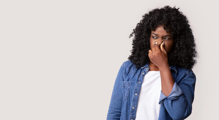 Portrait of black woman closing nose with fingers, feeling unpleasant scent, african american lady...