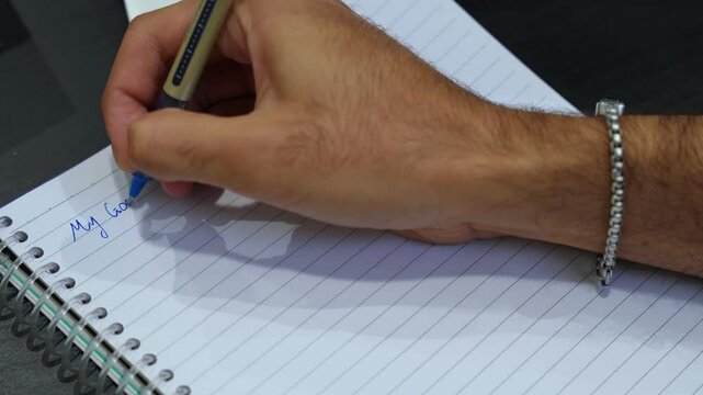 Close-up of hand writing “My Goals” in blue ink on spiral notebook. Ideal for motivation, productivity, planning, business strategy, or personal growth videos.