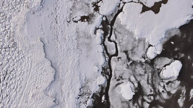 Aerial top-down view of frozen terrain meeting dark icy waters in Borgarfj&ouml;r&eth;ur, Iceland.