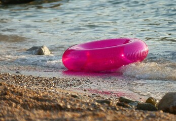 Pink plastic swim ring floating by the blue sea summer background
