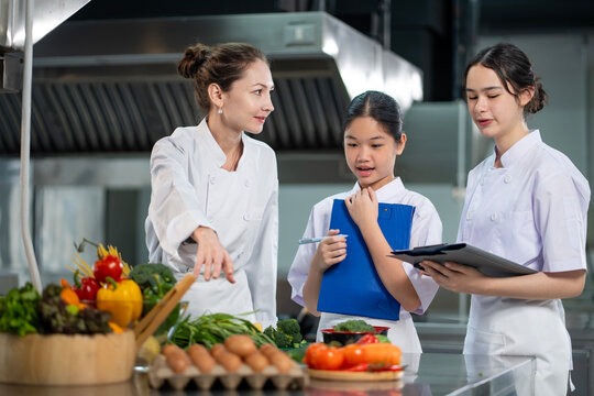 Professional chef is teaching young culinary class student to prepare fresh ingredient for the meal inside the restaurant kitchen for fine dining gourmet and cooking school