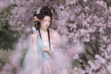 Young Asian woman in traditional dress among pink blossoms.