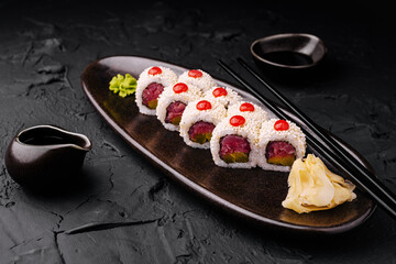Sushi rolls served on a black plate with ginger and wasabi