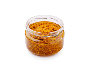 A clear jar filled with golden brown mustard seeds sits on a white surface