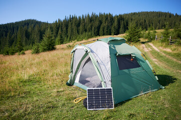 Green tourist tent pitched in grassy field with solar panel placed nearby.