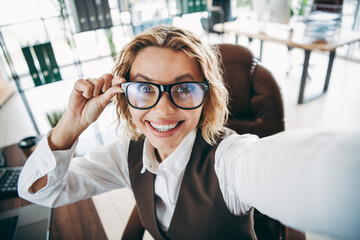 Confident businesswoman taking a cheerful selfie in stylish office attire at a modern workplace...