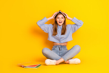 Young woman sitting cross-legged with book on head, expressing excitement on bright yellow...