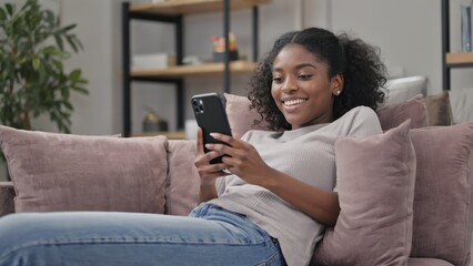 Obraz premium A smiling young woman relaxing on a couch with her cell phone.