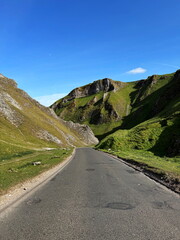 View of winding road through dramatic hills of Winnats Pass, England, UK, under a spring blue sky.
