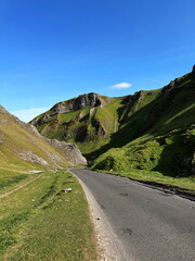 View of winding road through steep green hills in Winnats Pass, Peak District, England, under a...