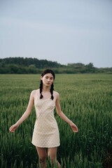 Young woman in a light dress standing in a green field.