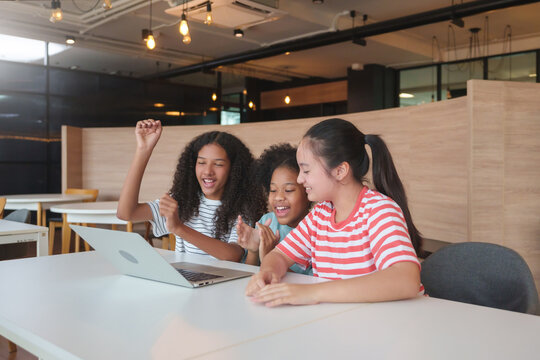Three joyful girls celebrating success while studying with a laptop together in a classroom, Multiethnic children showing excitement and the joy of learning through digital technology