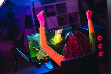 Joyful female gamer celebrates virtual gaming victory with lifted arms, enjoying an exciting...