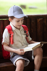happy little boy in cap sits in gazebo and reads book in summer