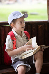 happy little boy in cap sits in gazebo and reads book in summer