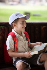 happy little boy in cap sits in gazebo and reads book in summer