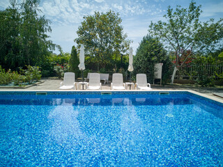 Clean outdoor pool with clear blue water, sun loungers, and umbrellas near modern apartment building. Peaceful summer vibe and relaxation area.