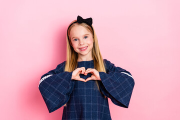 Young girl showing a heart gesture with hands on pink background and dressed in a stylish blue...