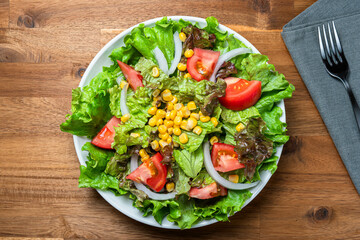 Fresh green salad with lettuce, tomato and corn on a white plate