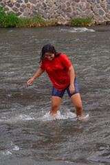 A teenage girl steps carefully through the center of the river, confidently walking across the strong flowing water with focused determination.