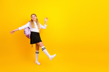 Fototapeta na wymiar Happy student girl celebrating school success on bright yellow background with backpack and uniform skirt, joyful mood