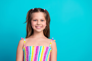 Charming young girl in colorful dress posing against vibrant turquoise background, radiating joy...