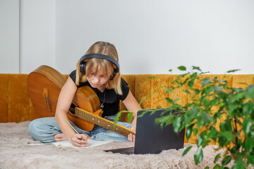 Girl studying music online with guitar and headphones. Copy space