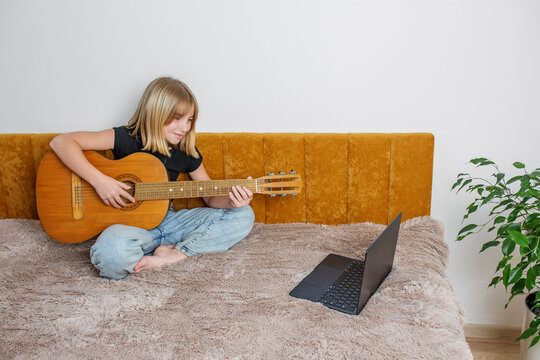 Smiling preteen girl learning guitar online. Copy space