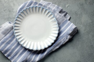 A spotless white plate with a blue rim sits on a striped cloth atop a textured grey background