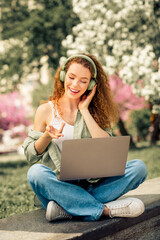 Young woman enjoying music while working outdoors in a park on a sunny day during spring or summer