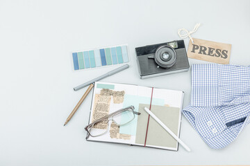 Flat lay of retro journalist essentials on blue background: camera, press badge, notebook
